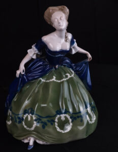 Porcelanowa figurka kobiety ubranej w niebiesko zieloną suknię balową.