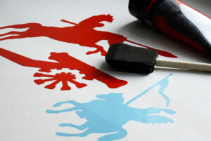 Czerwone malunki przedstawiające armatę i szarżującego husarza. Obok niebieski rysunek husarza. 