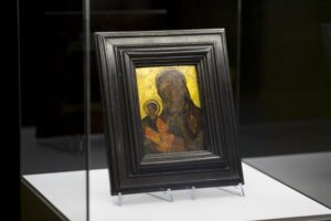 Zbliżenie na ikonę Matki Boskiej. Ikona w brązowej ramie, tło żółte. Matka Boska i dzieciątko Jezus w ciemnych odcieniach.