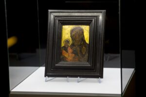 Zbliżenie na ikonę Matki Boskiej. Ikona w brązowej ramie, tło żółte. Matka Boska i dzieciątko Jezus w ciemnych odcieniach.