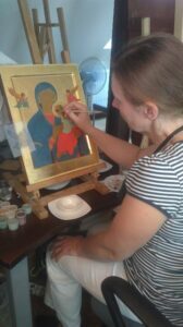 Kobieta pisząca ikonę. Ikona koloru złotego, przedstawia Matkę Boską.