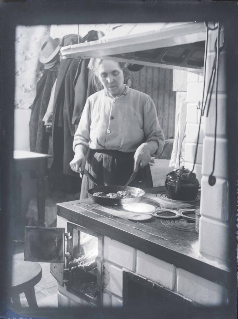 Fotografia czarno-biała. W kuchni stoi kobieta i przygotowuje potrawę
