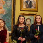 Trzy młode kobiety z kwiatami w ręku stoją na tle obrazów na galerii malarstwa